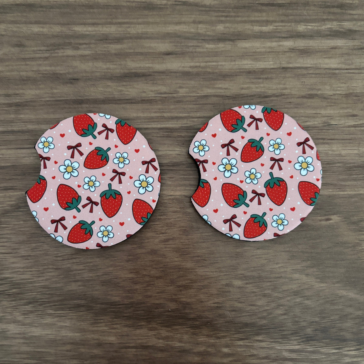 Two round fabric car coasters with a strawberry and flower pattern, displayed on a dark wood background.