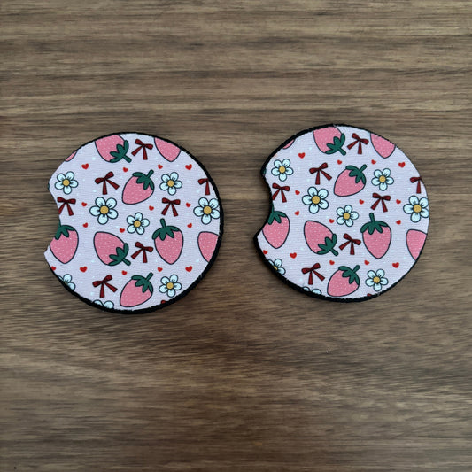 Two round fabric pieces with a strawberry and flower pattern, placed side by side on a wooden surface.