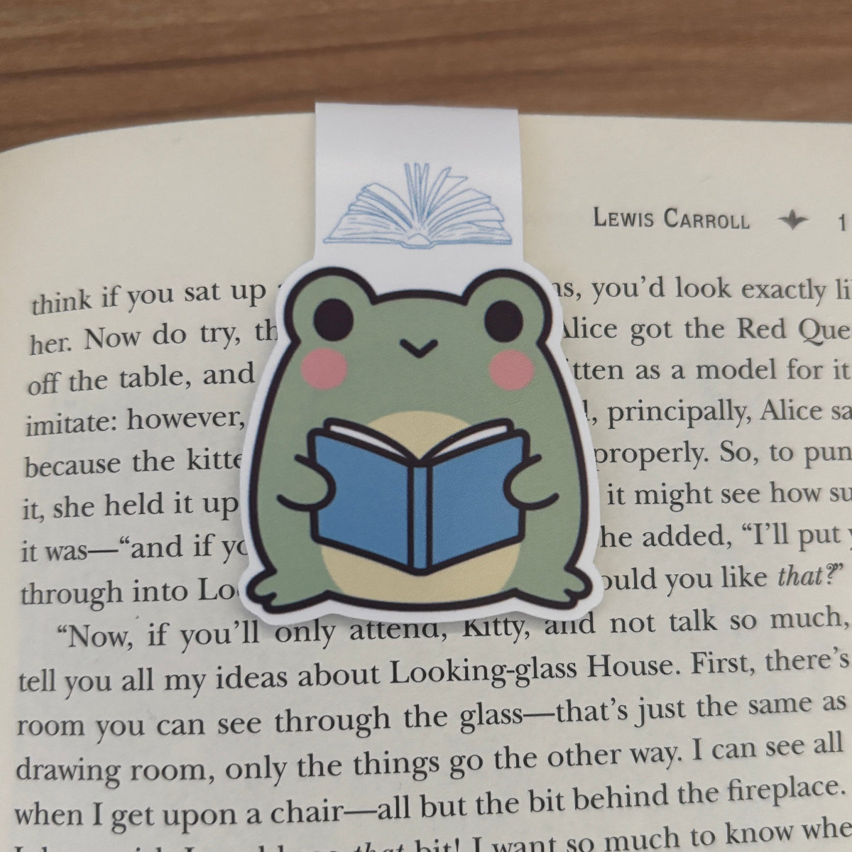 Frog-shaped bookmark reading a book on an open book with text.