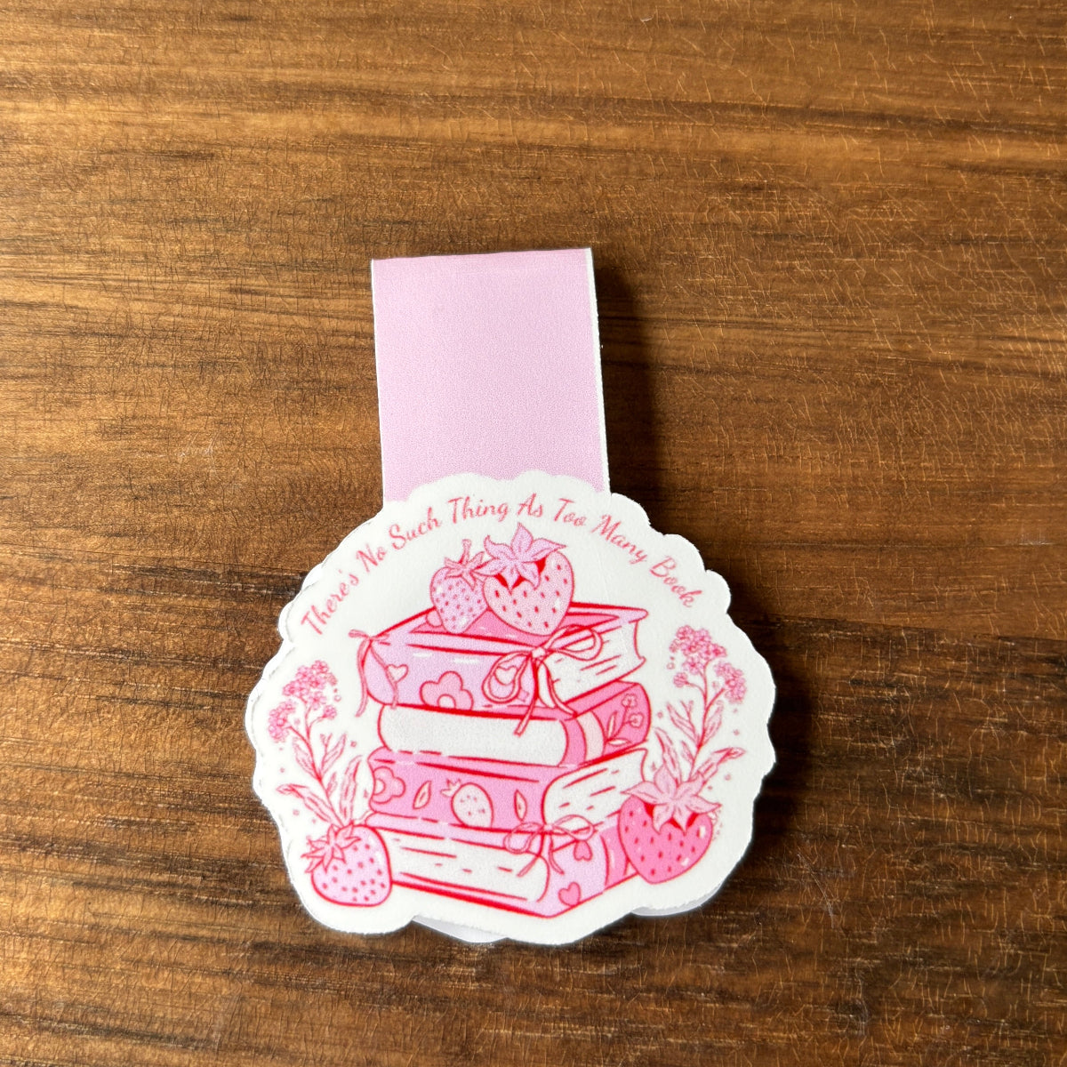 Pink magnetic bookmark with book and strawberry design on a wooden surface