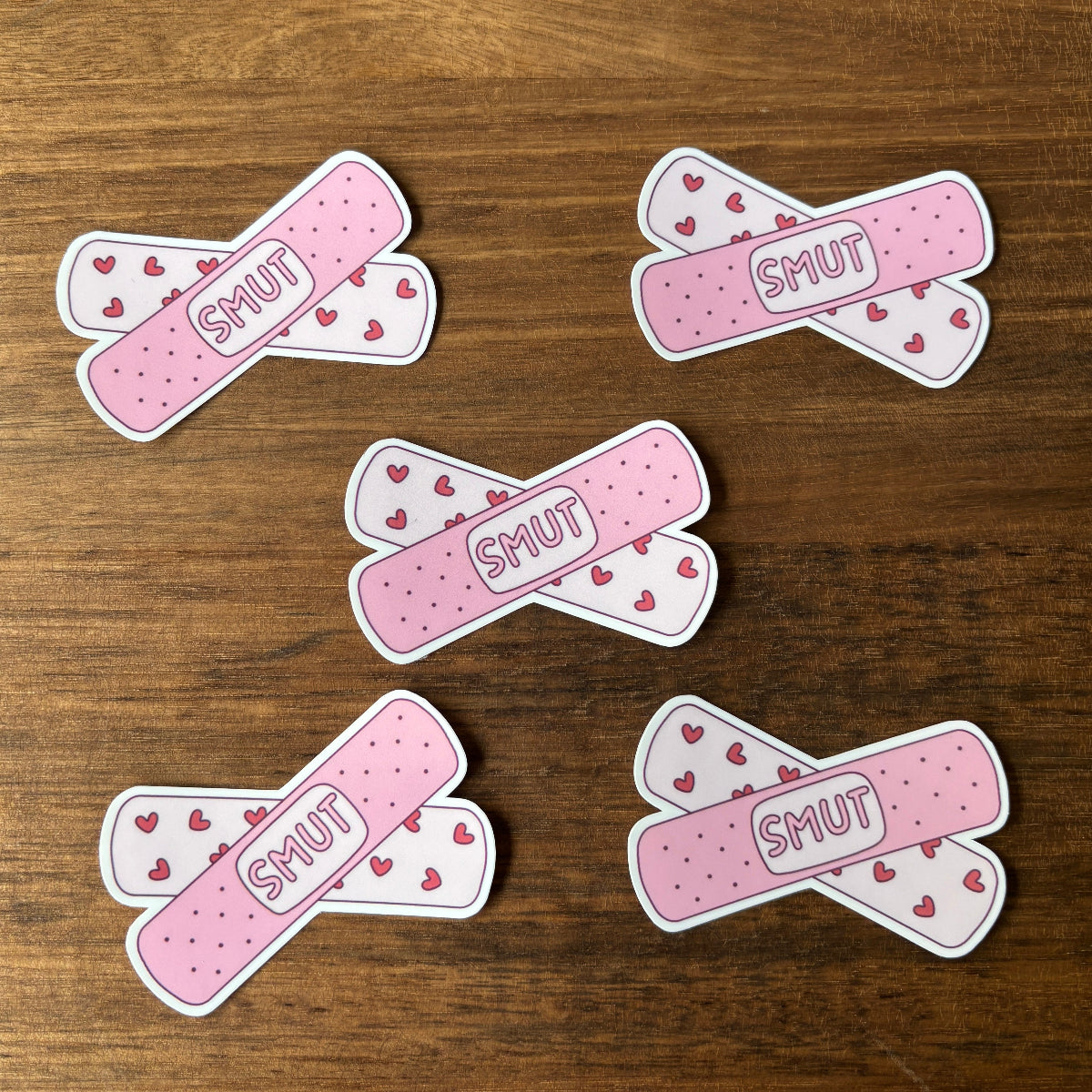 Pink bandage-shaped stickers with 'SMUT' text on a wooden surface