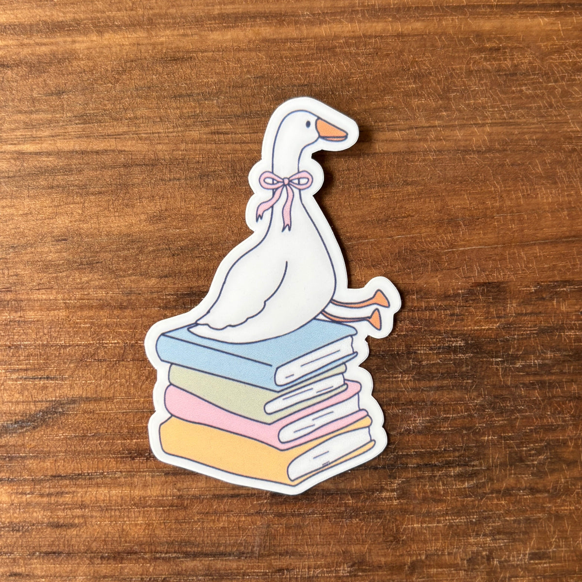 Sticker of a goose with a bow on books on a wooden surface