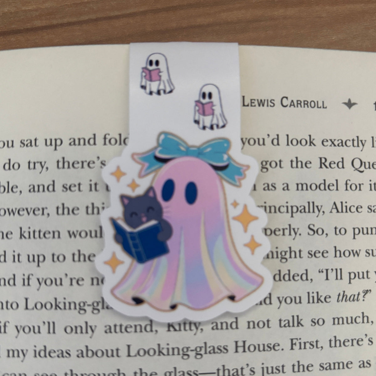 Ghost character with a bow and cat reading a book on a bookmark with Lewis Carroll text.