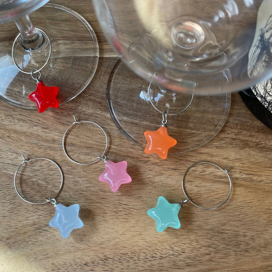 A collection of silver wine glass charm rings with star charms attached to them, displayed on a wooden surface.
