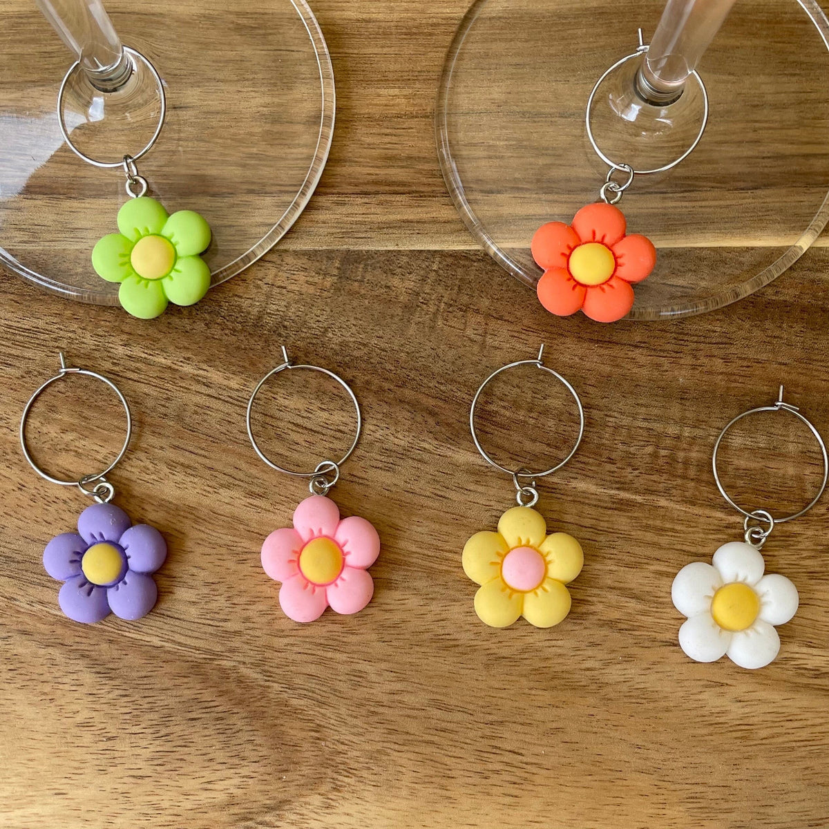Silver wine glass charms with colorful resin flower charms in purple, pink, yellow, white, green, and orange placed on a wooden surface.