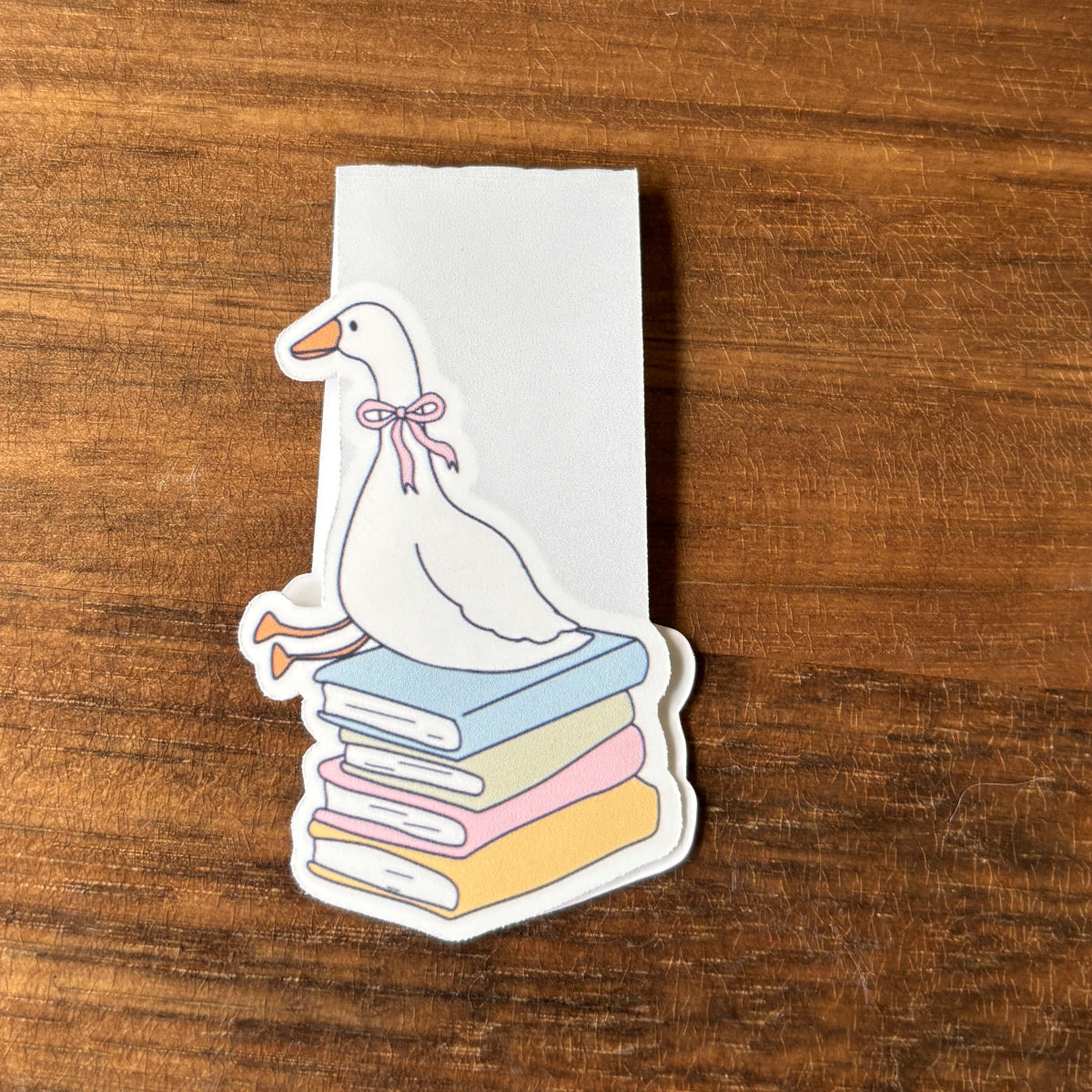 magnetic bookmark  of a duck on books with a bow on a wooden surface