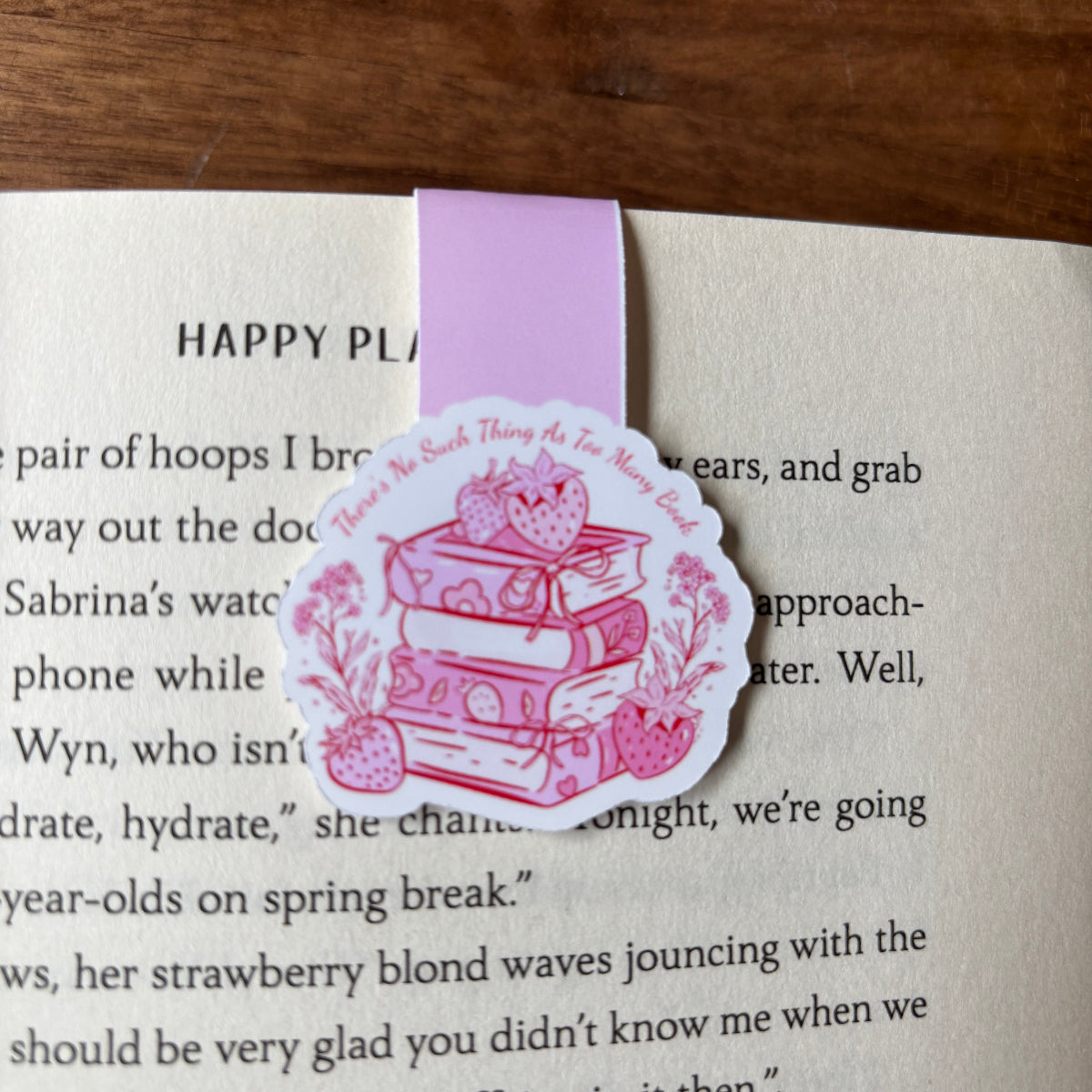 Pink bookmark with a design of books and a strawberry on a book page.