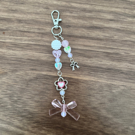 A pastel pink and iridescent beaded charm keychain with a silver lobster clasp, resting on a brown wooden surface.